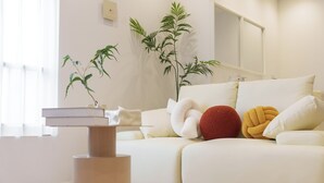 A modern living room with a sofa, decorative pillows, a small table, and two potted plants. - TORA HOTEL Sumidagawa (Tokyo)