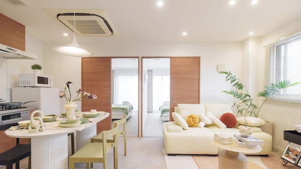 A modern living room with a sofa, coffee table, and dining area with chairs and a microwave. - TORA HOTEL Sumidagawa (Tokyo)