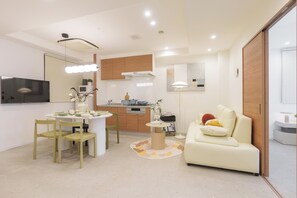 Ein modernes Wohnzimmer mit Sofa, Esstisch, Stühlen und einer Küchenzeile mit Schränken und Geräten.