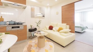 A modern living room with a sofa, a dining table, and a kitchen area with a stove. - TORA HOTEL Sumidagawa (Tokyo)