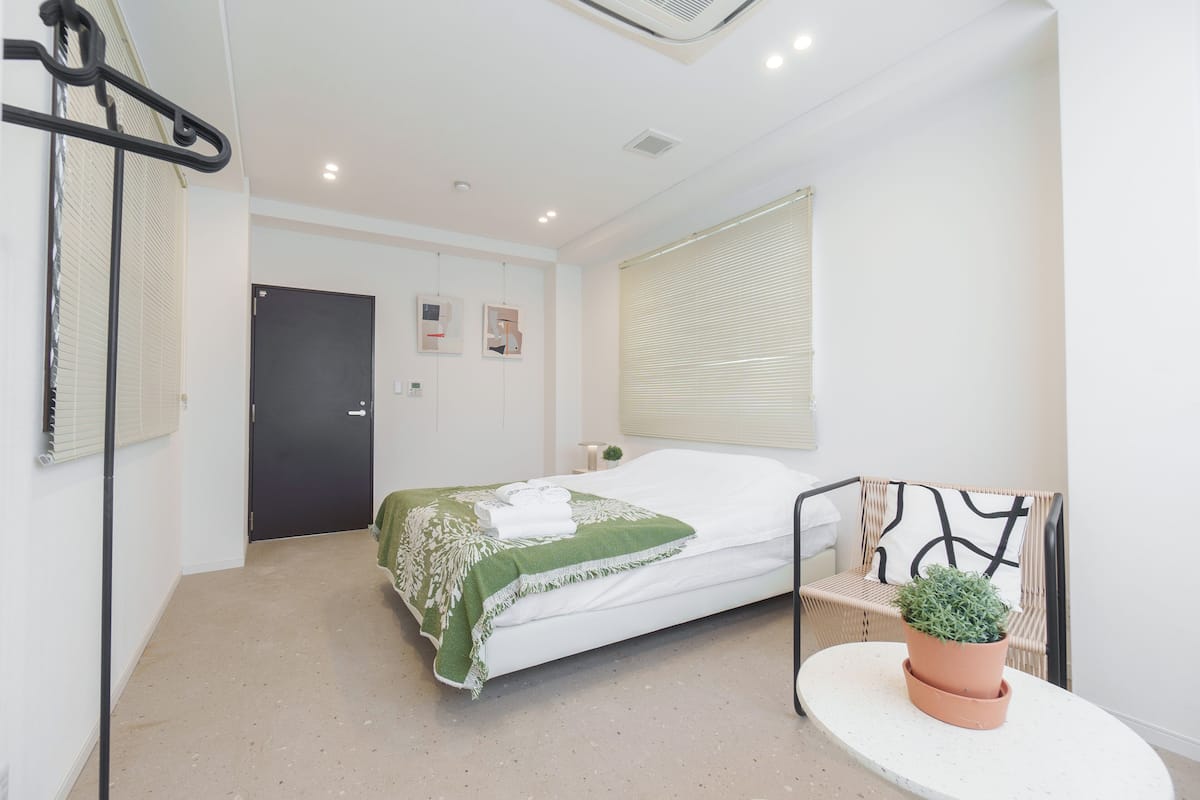 Ein Schlafzimmer mit einem Bett, einer Zimmerpflanze, einem Sessel und einer Tür.