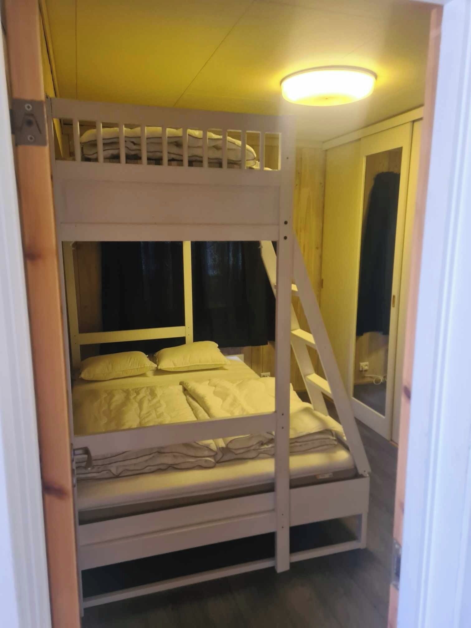 A bunk bed with a lower bunk and a top bunk, both with white bedding. There is a window with a curtain on the lower bunk.