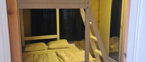 A bunk bed with a lower bunk and a top bunk, both with white bedding. There is a window with a curtain on the lower bunk.