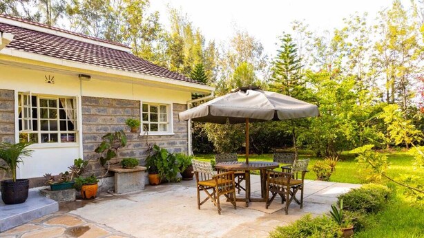 A house with a stone patio, a table with chairs, and an umbrella.