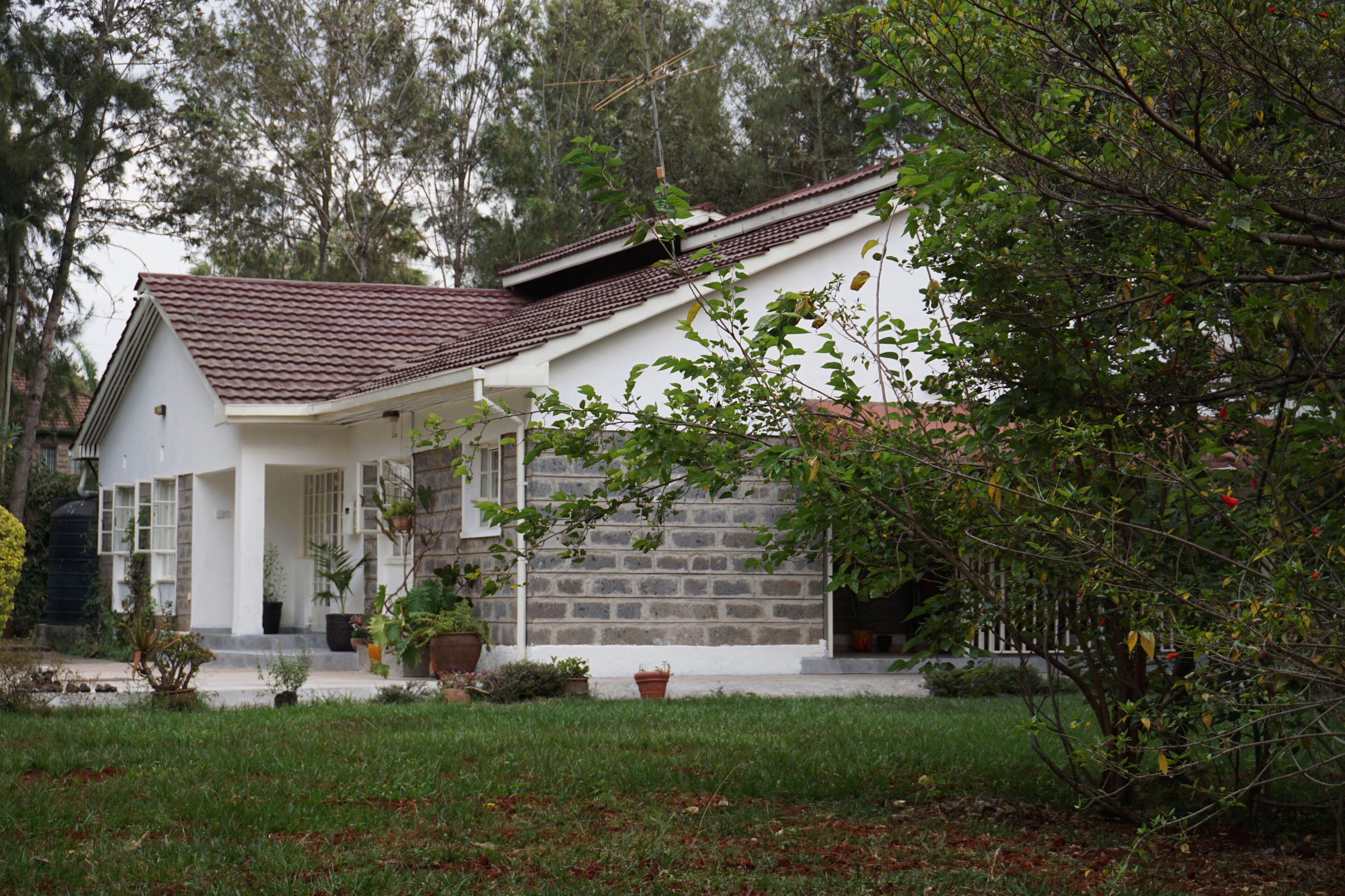 A house with a sloped roof, a stone wall, and a front porch with potted plants.