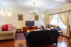 A living room with a sofa, armchair, TV, and artwork on the wall. - 3-bedroom standalone home,spacious garden with daybed,located in Karen, Nairobi. (Nairobi)