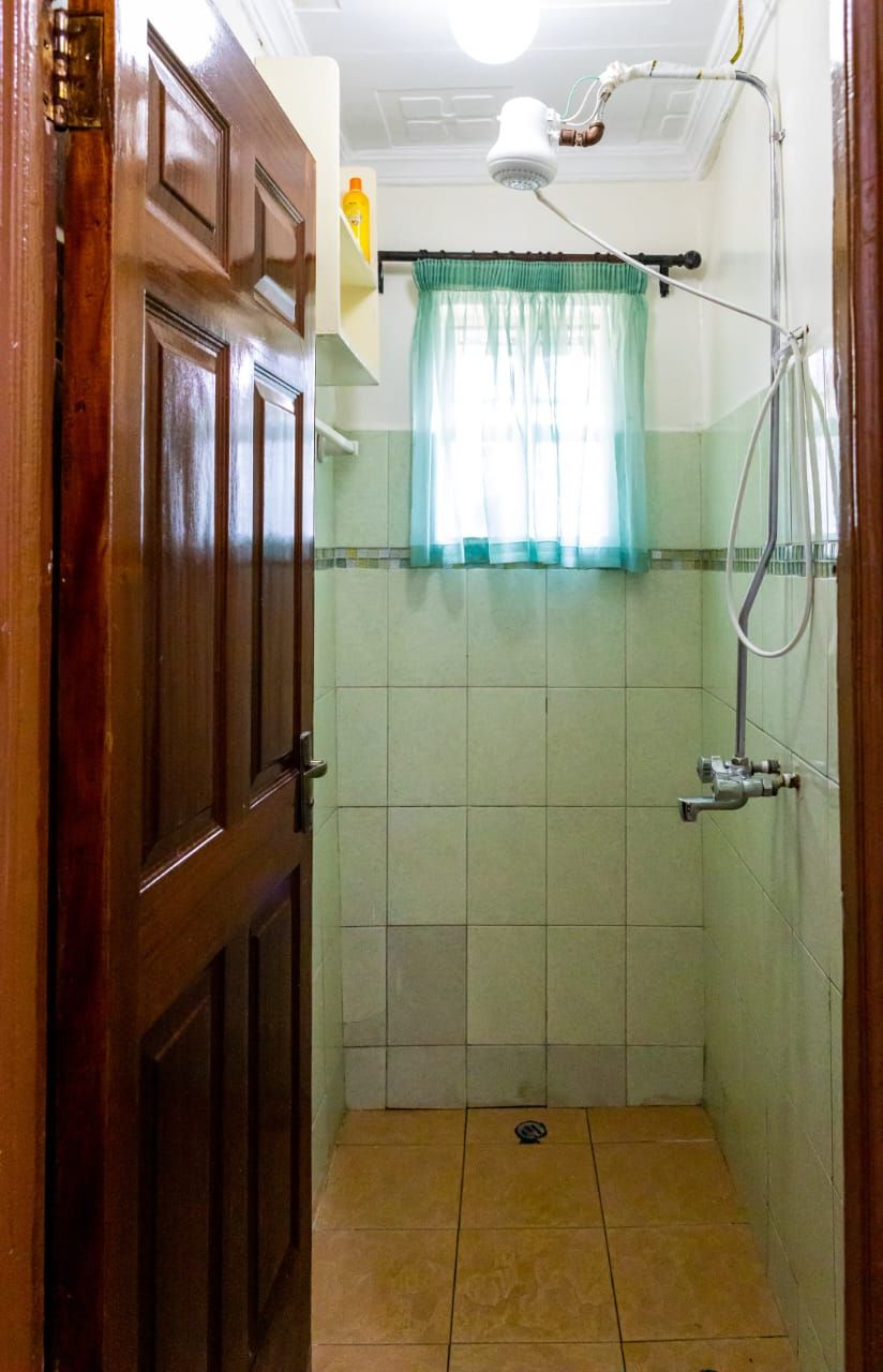 A small, tiled shower room with a wooden door, a showerhead, and a curtain.
