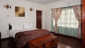A bedroom with a bed, a wooden bench, a ceiling fan, a door, and a window with floral curtains.