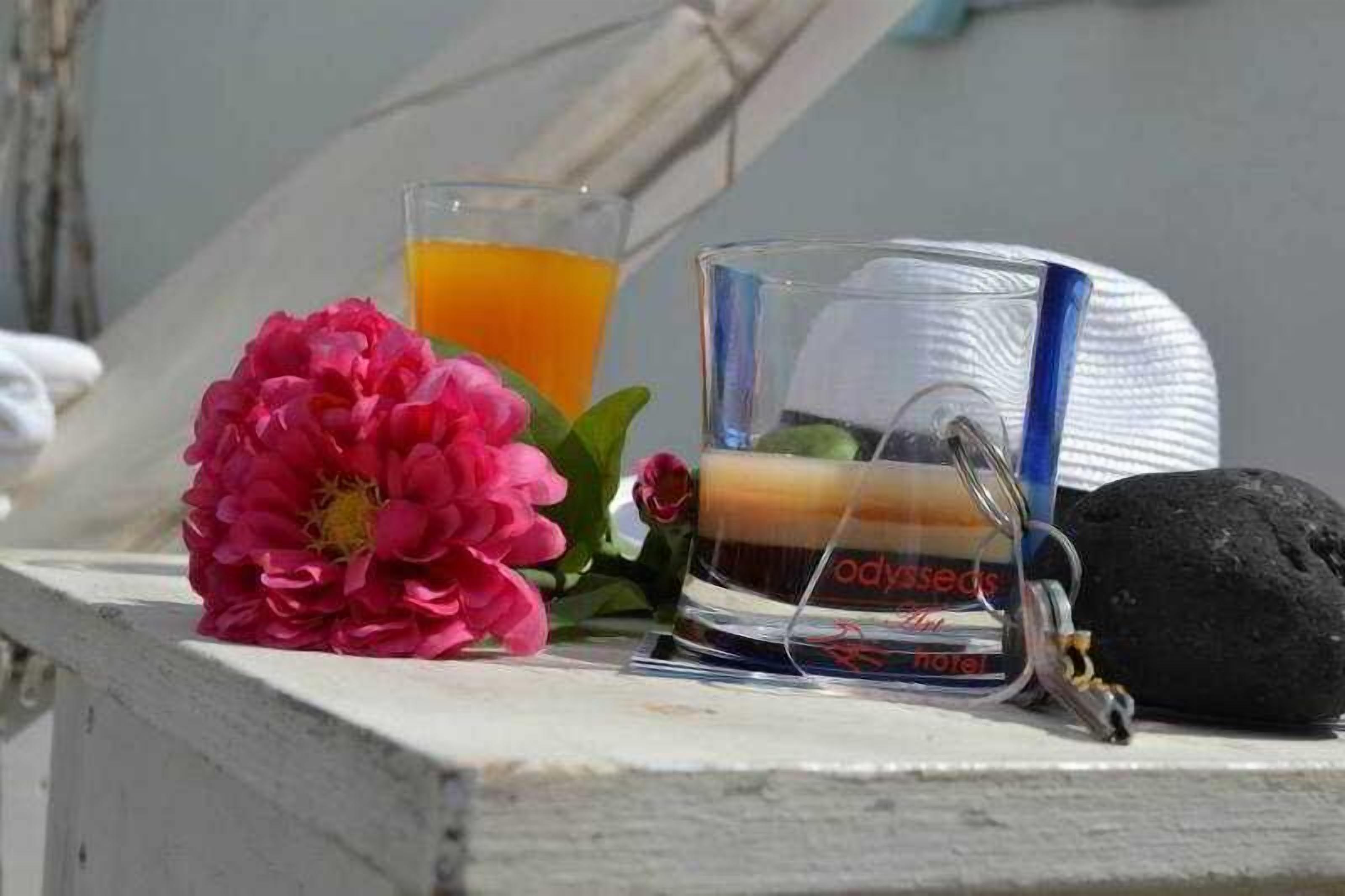 A glass of orange juice, a pink flower, and a bottle of water on a white surface.