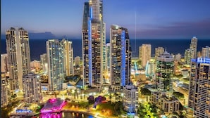 A cityscape with high-rise buildings, a waterfront, and a brightly lit area with colorful lights. - Sub-Penthouse Dream in Circle on Cavill (Gold Coast)