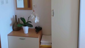 Ein kleiner Raum mit Schreibtisch aus Holz, einem Spiegel, einer Topf-Orchidee und einem Kleiderschrank.