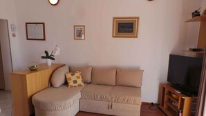 Ein Wohnzimmer mit Sofa, Hocker, Couchtisch aus Holz und einem Fernseher auf einem Holzboden.