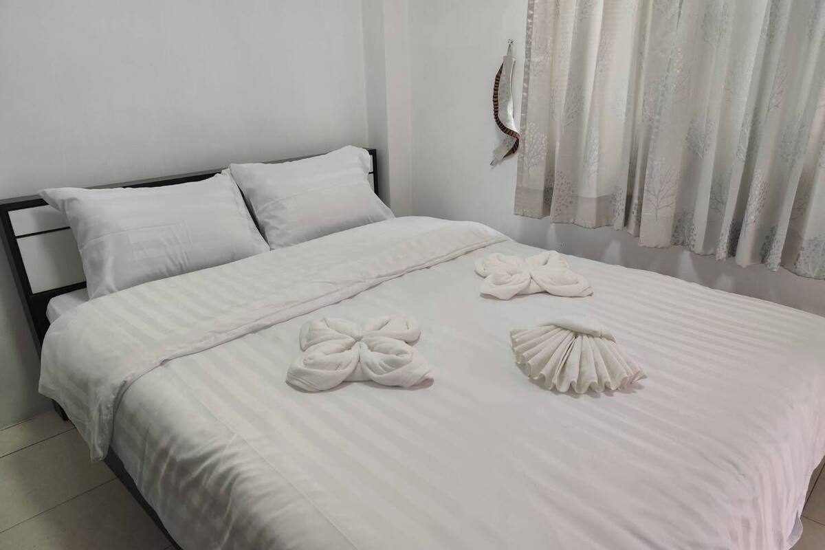A neatly made bed with white linens and two towels arranged on the bed.