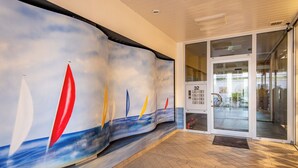A modern building entrance with a mural of sailboats on the wall, a glass door entrance, and a tiled floor.