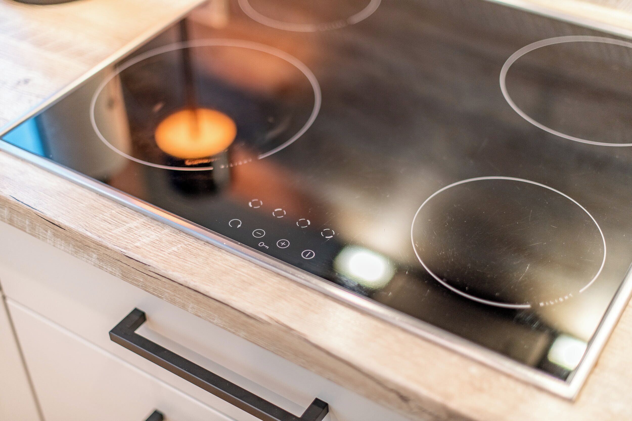 A modern kitchen with a glass stovetop, wooden cabinets, and a stainless steel range hood.