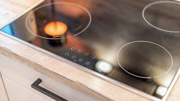 A modern kitchen with a glass stovetop, wooden cabinets, and a stainless steel range hood.