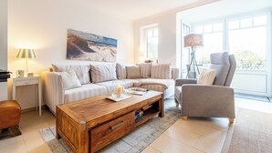 A modern living room with a sofa, armchair, coffee table, and a painting on the wall.