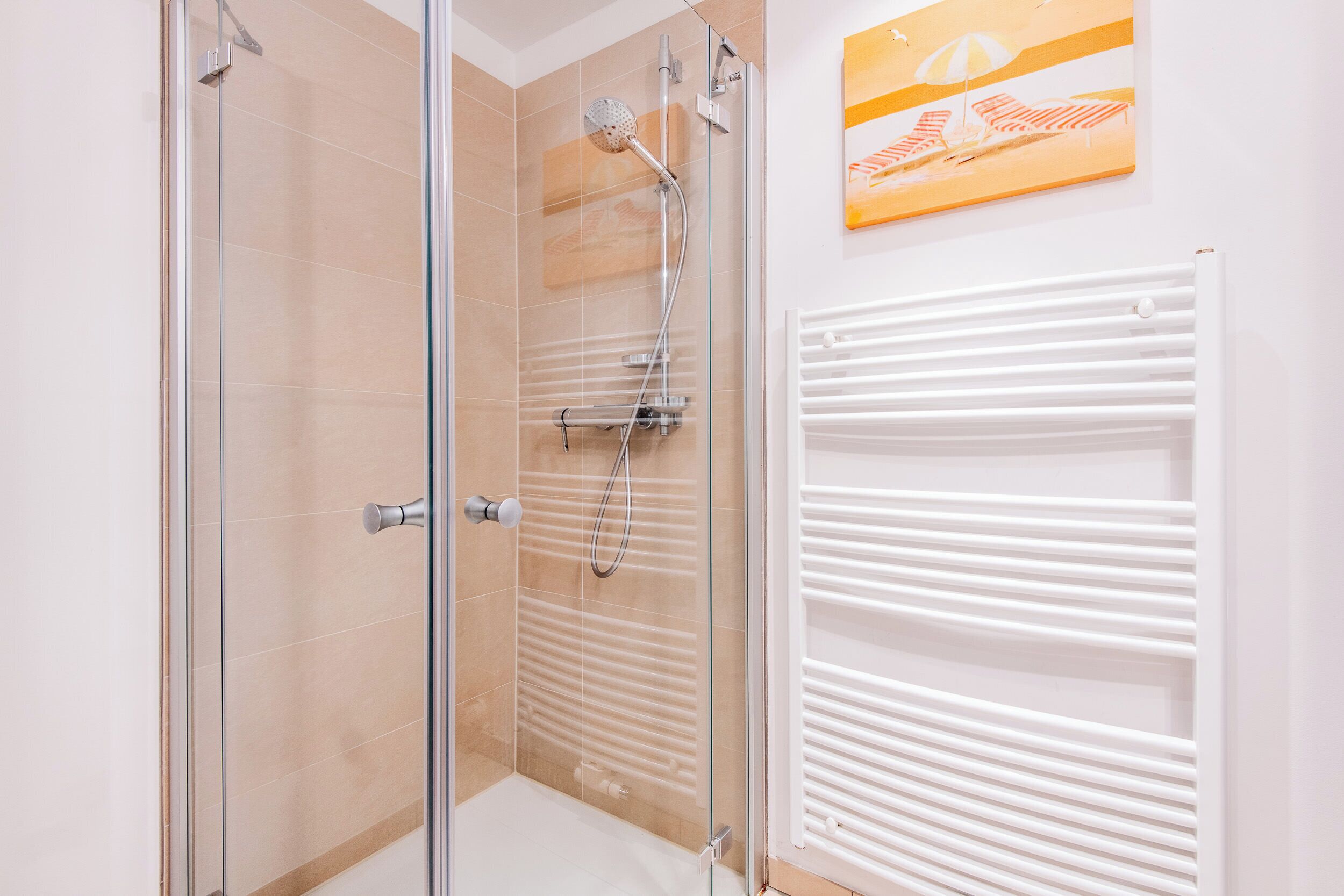 A glass-enclosed shower with a white radiator and a beach-themed painting on the wall.