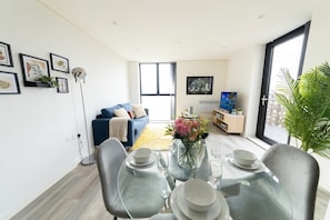 A modern living room with a dining area, a sofa, a TV, and a large window.