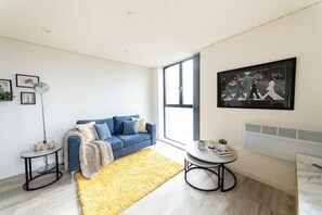 A modern living room with a blue sofa, a yellow rug, a round table, and a large window. - Modern & Bright Central Liverpool 1 Bed Apartment (Liverpool)