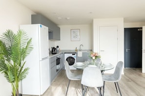 A modern kitchen with a refrigerator, oven, and sink, a dining area with a table and chairs, and a potted plant.