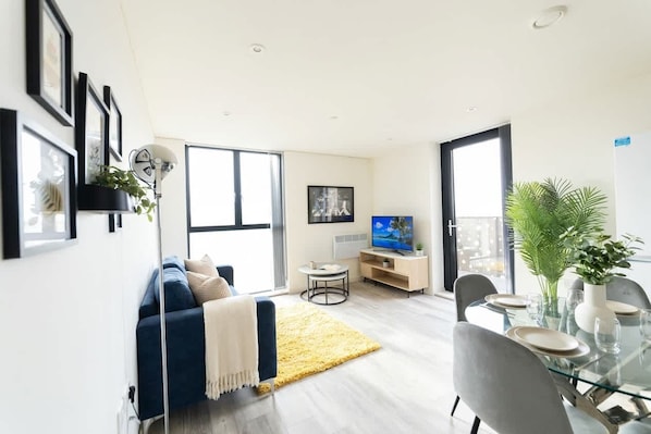 A modern living room with a sofa, a glass dining table, and a television.