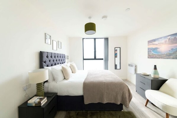 A modern bedroom with a large bed, bedside tables, a chair, and a window with a view. - Modern & Bright Central Liverpool 1 Bed Apartment (Liverpool)
