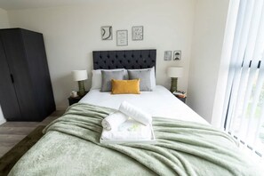 A bedroom with a bed, bedside lamps, a wardrobe, and artwork on the wall.
