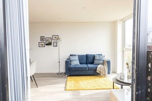 A modern living room with a blue sofa, a yellow rug, and a floor lamp.