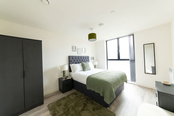 A modern bedroom with a large bed, a wardrobe, a bedside table, a lamp, and a window.
