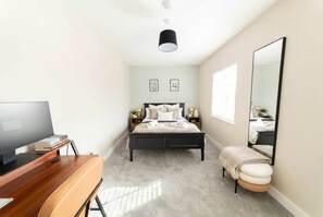 A bedroom with a bed, a desk with a computer, a chair, a bedside table with lamps, a large mirror, and a window. - Chic City-Centre Apartment with 1 Bedroom (Liverpool)