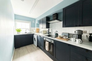 Une cuisine moderne avec des meubles de rangement de couleur sombre, un lave-linge, une machine à café et un grille-pain.