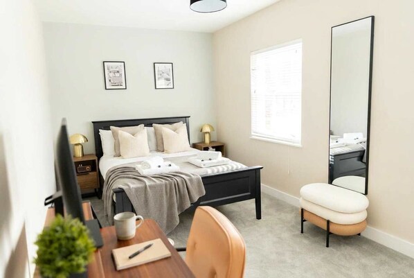 Une chambre à coucher comprenant un lit, des tables de chevet, un bureau, une chaise, un miroir et une fenêtre.