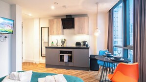 Moderni hotellihuone, jossa on pieni keittiö, ruokailutila ja suuri ikkuna, jossa on verhot.