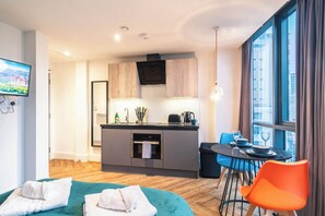 Ein modernes Hotelzimmer mit einer Küchenzeile, einem Essbereich und einem großen Fenster mit Vorhängen.