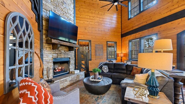 A spacious living room with a stone fireplace, a large flat-screen TV, and a cozy seating area with a leather couch and armchairs. - Games, Hot Tub, Fire Pit, Pets, Times Like These (Broken Bow)