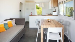 A modern kitchen with white cabinets, a wooden dining table, and a built-in oven. - Beach Apartments (Olbia)