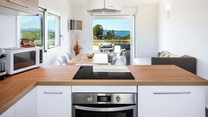 A modern kitchen with a wooden countertop, built-in microwave, and oven. There is a dining area with a table and chairs, and a balcony with a view of the sea. - Beach Apartments (Olbia)