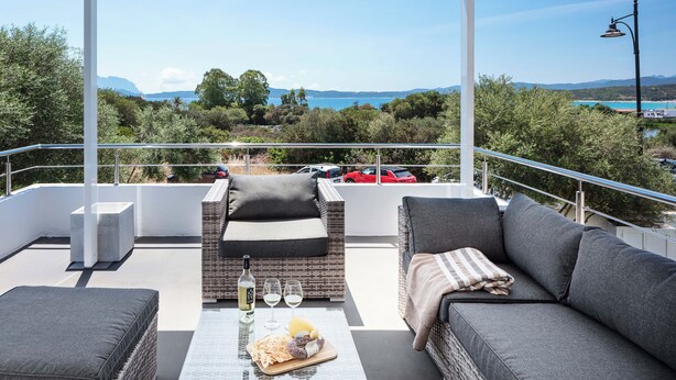 A rooftop terrace with a view of the sea, furnished with a sofa, a table with a bottle and glasses, and a small seating area. - Beach Apartments (Olbia)