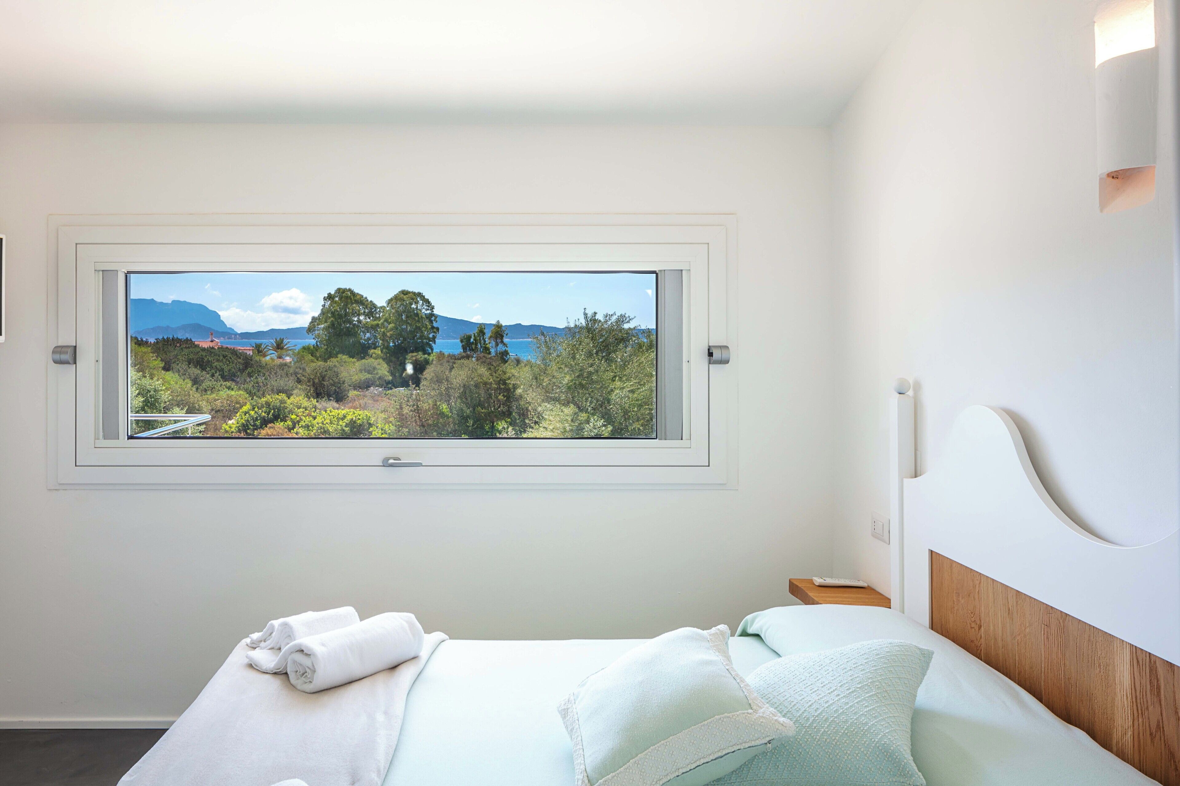 A bedroom with a large window offering a scenic view of greenery and mountains.