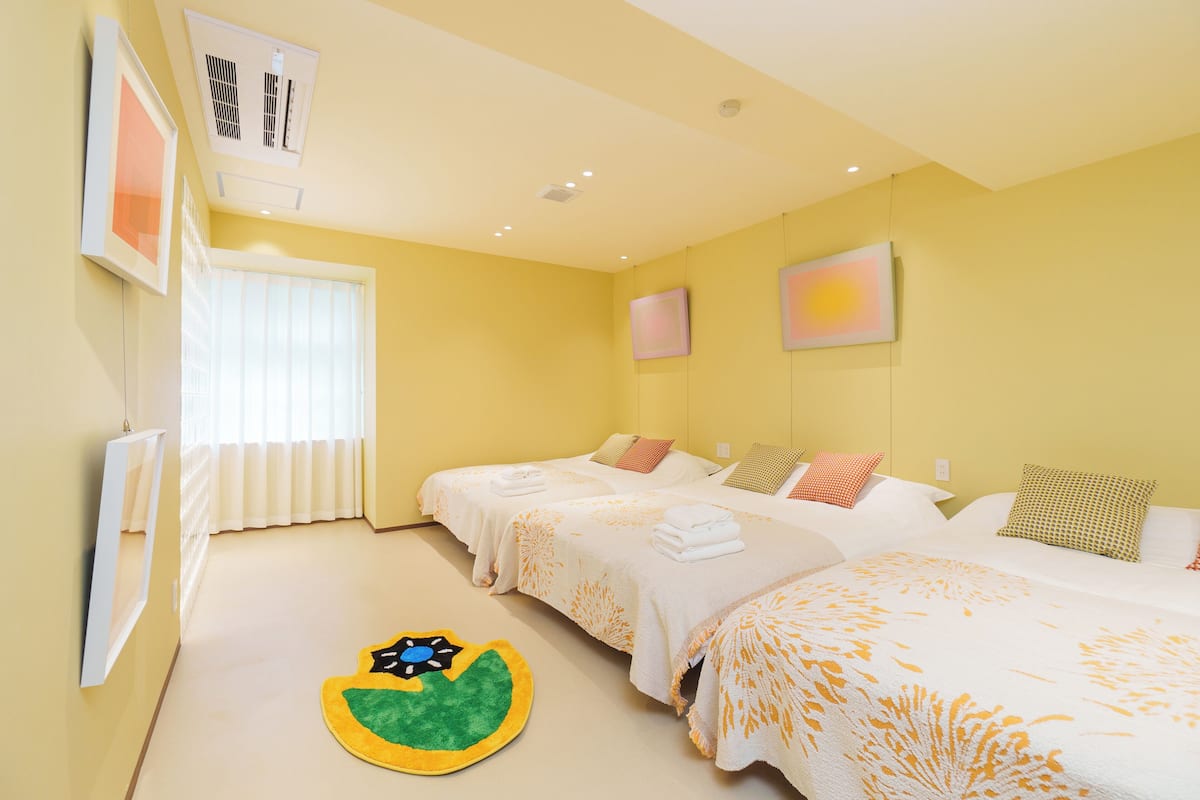 A hotel room with two beds, a window with blinds, a radiator, and artwork on the walls.