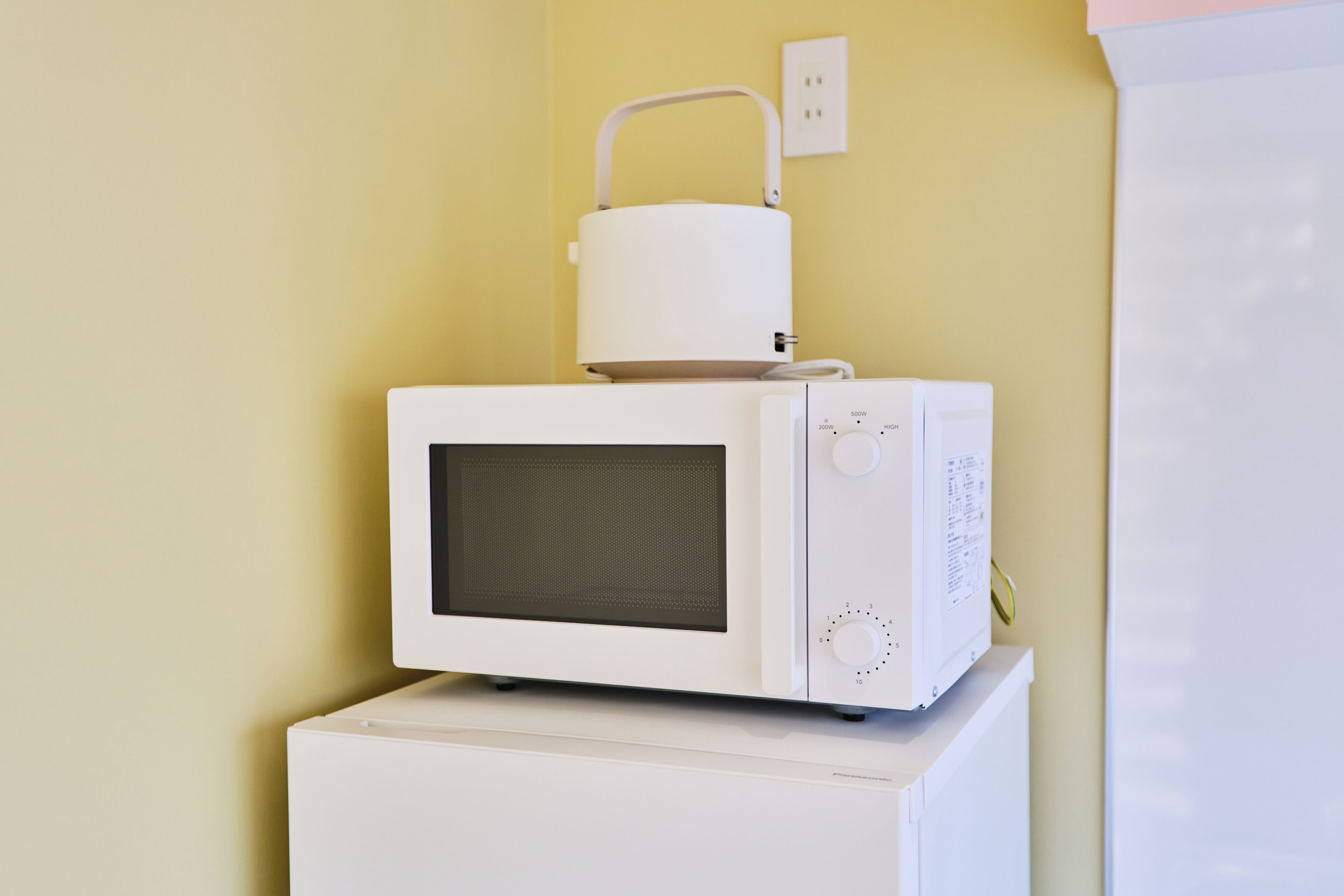A white microwave oven on top of a white appliance, likely a refrigerator, against a yellow wall.