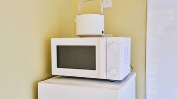 A white microwave oven on top of a white appliance, likely a refrigerator, against a yellow wall.