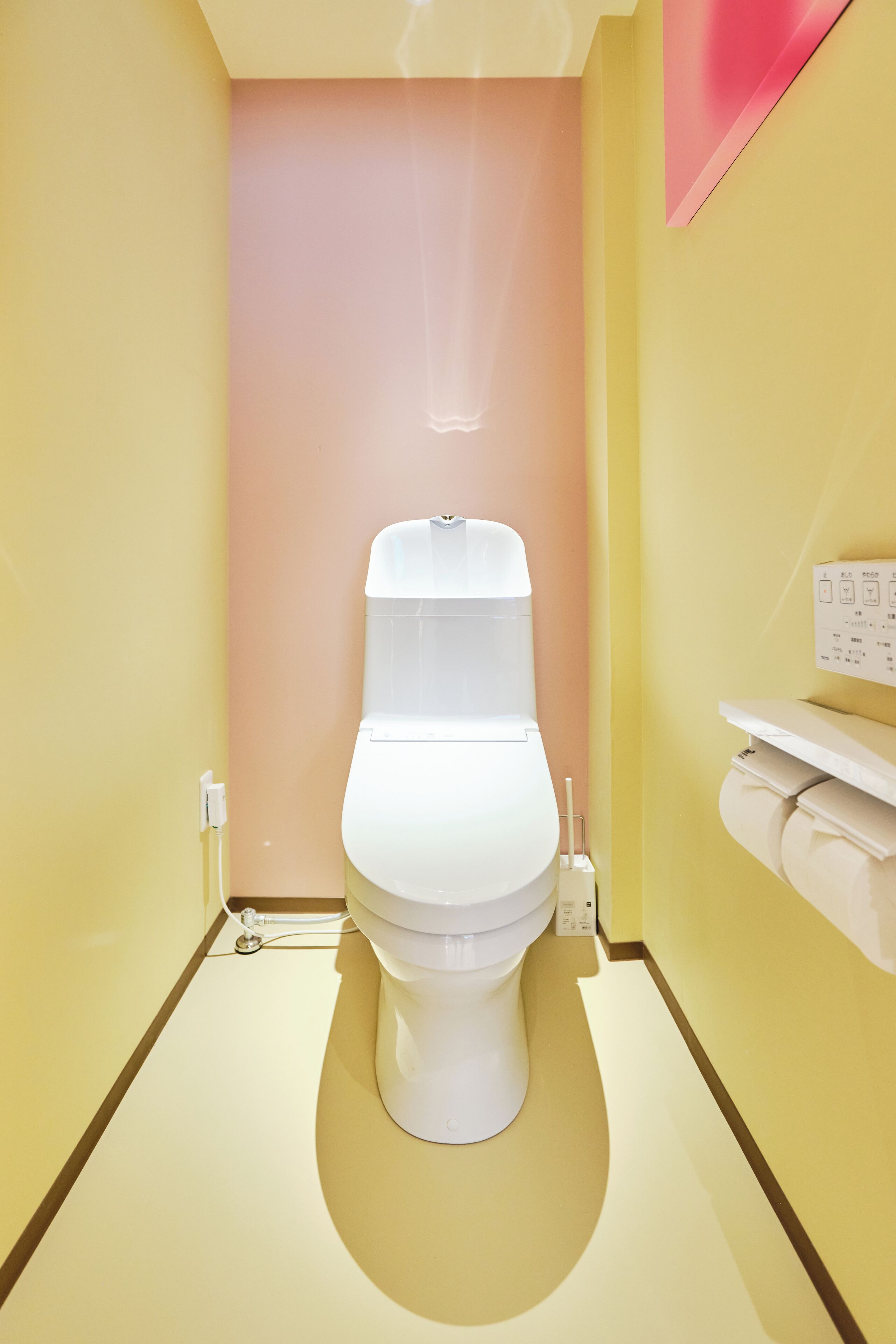 A modern bathroom with a white toilet, a wall-mounted toilet paper holder, and a visible electrical outlet.