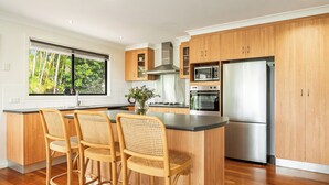 Een moderne keuken met houten kastjes, een roestvrijstalen koelkast, een inbouwoven en een groot raam met uitzicht op groen.