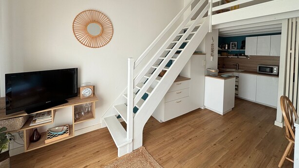 Ein modernes Wohnzimmer mit Treppe, einer Küche und einem Flachbildfernseher.