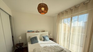 Ein Schlafzimmer mit Bett, Nachttisch, Lampe, Pendelleuchte und einem Fenster mit Vorhängen.
