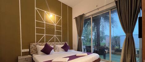 A bedroom with a bed, a nightstand, a wall-mounted light, and a view through a glass door.
