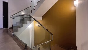 Een moderne trap met glazen leuning en metalen handrail, die uitkomt op een plateau met een lamp.