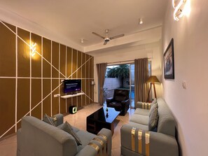 Uma sala de estar moderna com uma televisão de tela plana, um ventilador de teto e um conjunto de sofás.